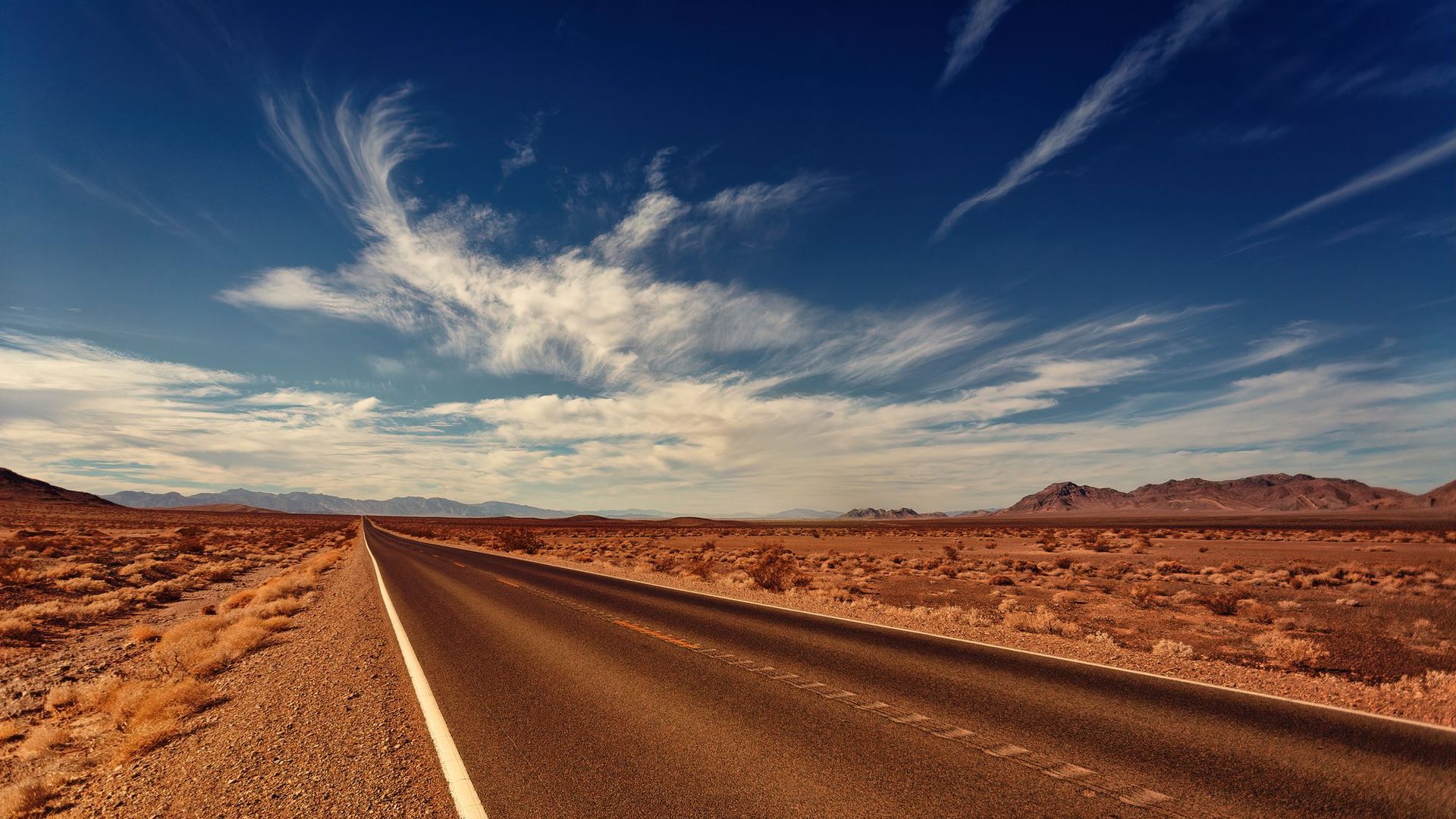 An empty highway stretching into a sunbaked desert toward distant mountains
